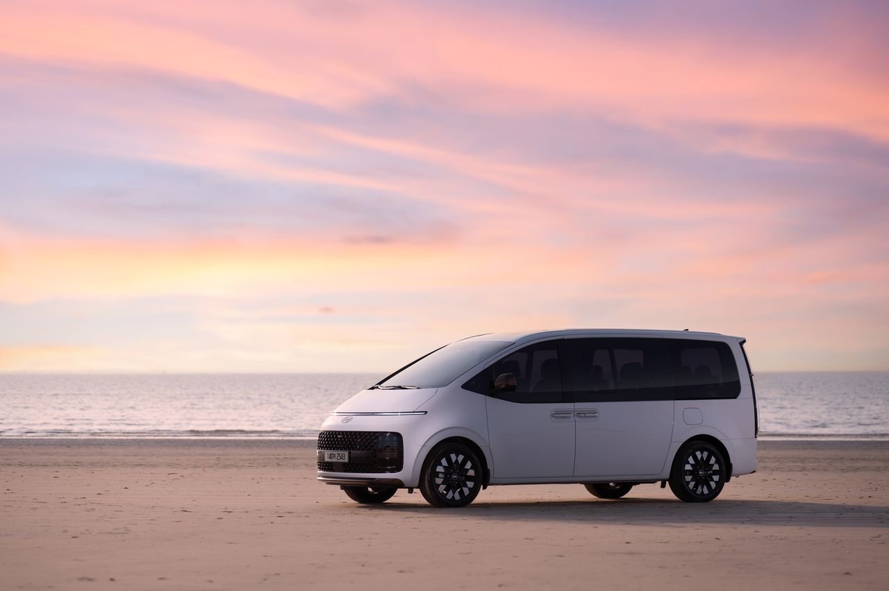 A white minivan on a sandy beach with a stunning pink sunset backdrop.