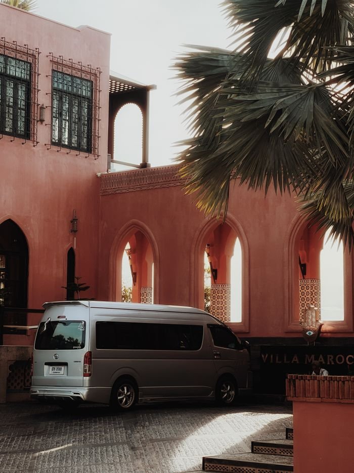 Home A minivan parked in a charming Moroccan courtyard with pink walls and decorative arches.