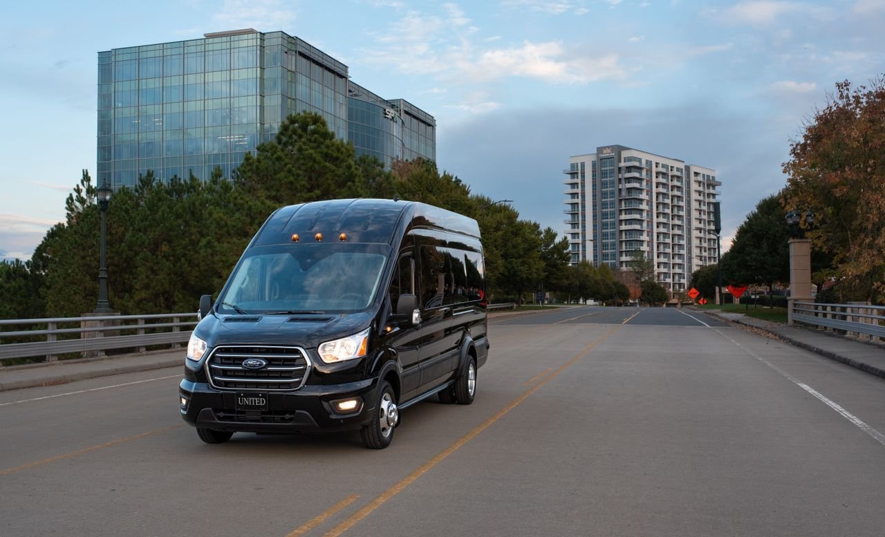 A sleek black minivan travels down an empty city road surrounded by modern buildings.