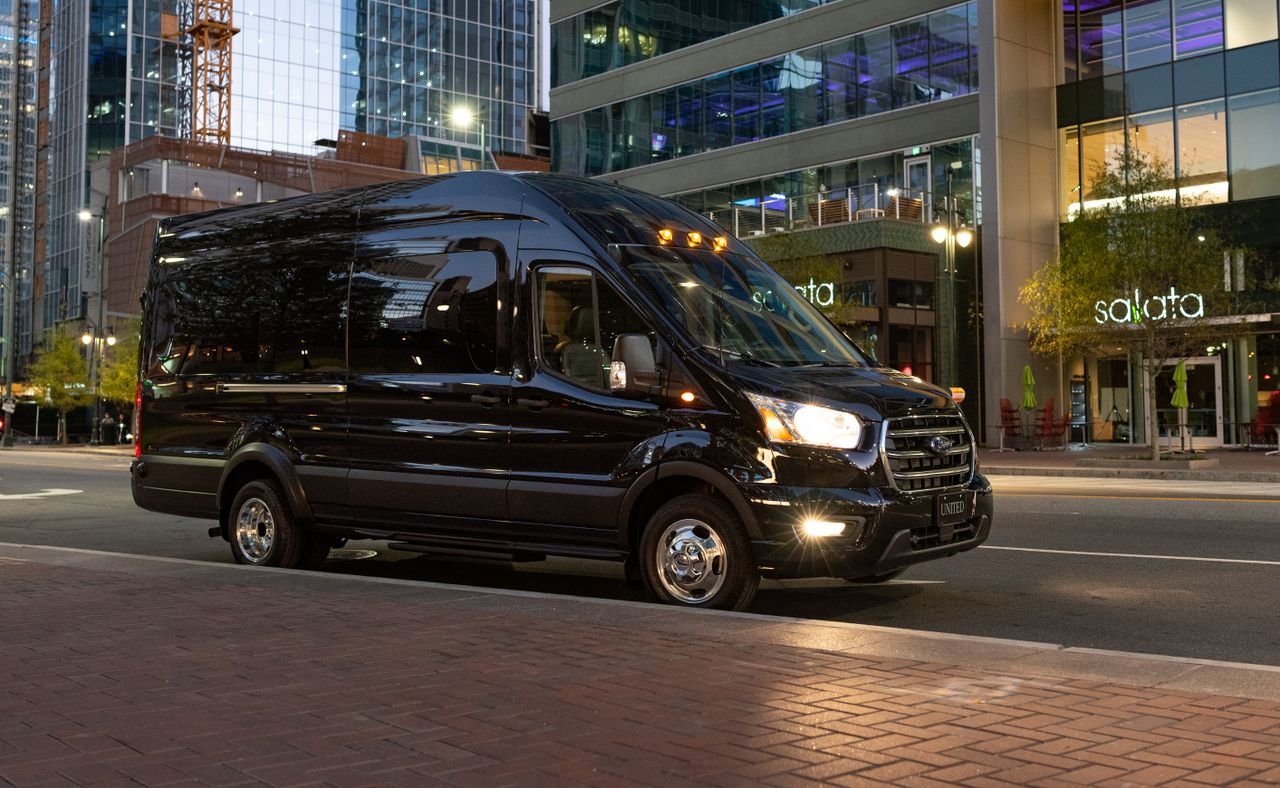 Black van parked in a modern city environment at dusk, with skyscrapers and urban elements.